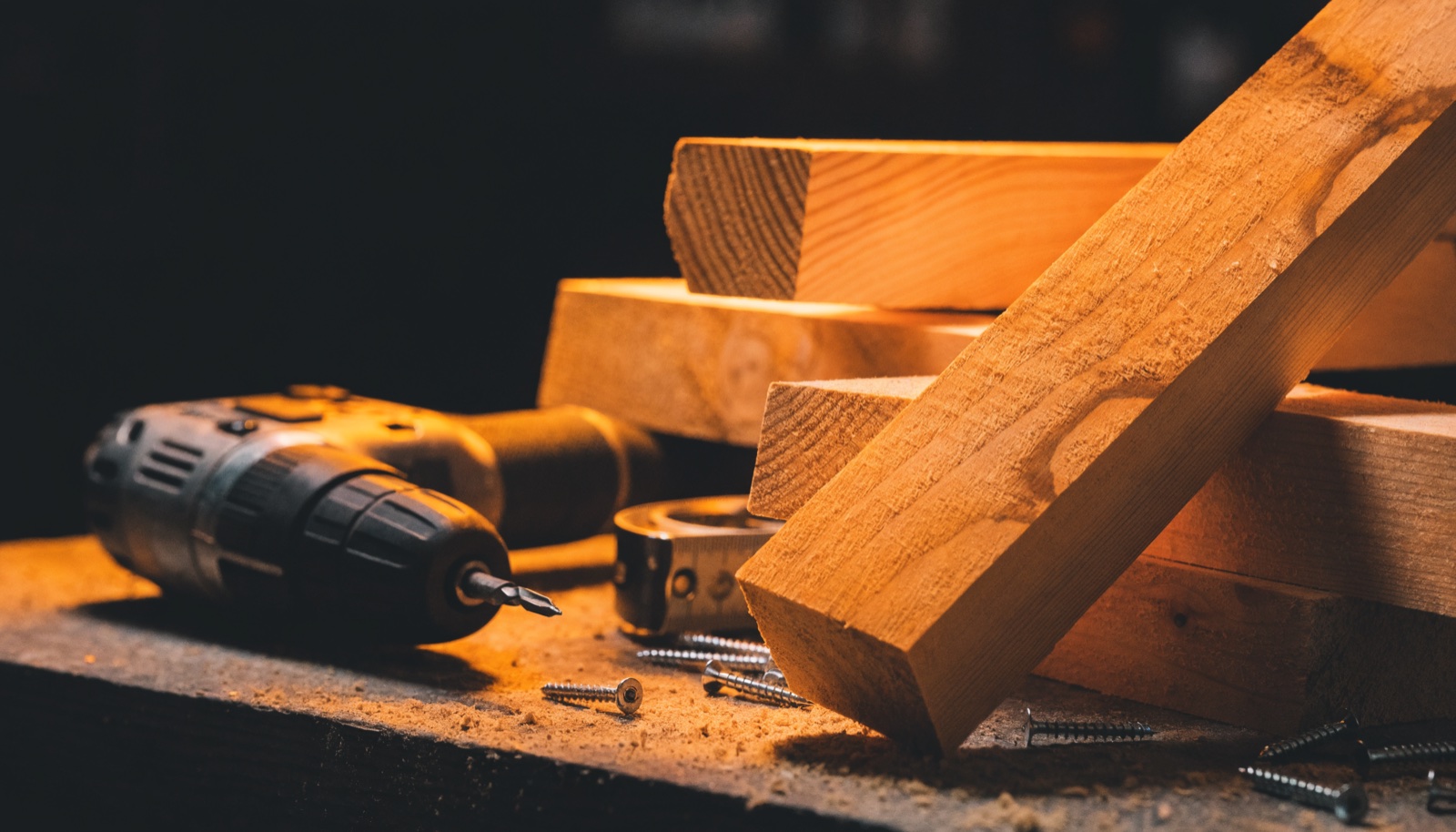 A cordless driver, screws and dressed timber lengths lit on a workbench