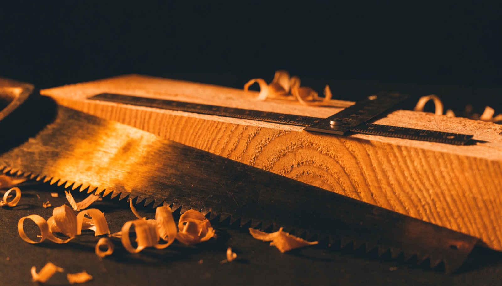 A hand saw and a steel square resting on a sawn timber board with curled shavings
