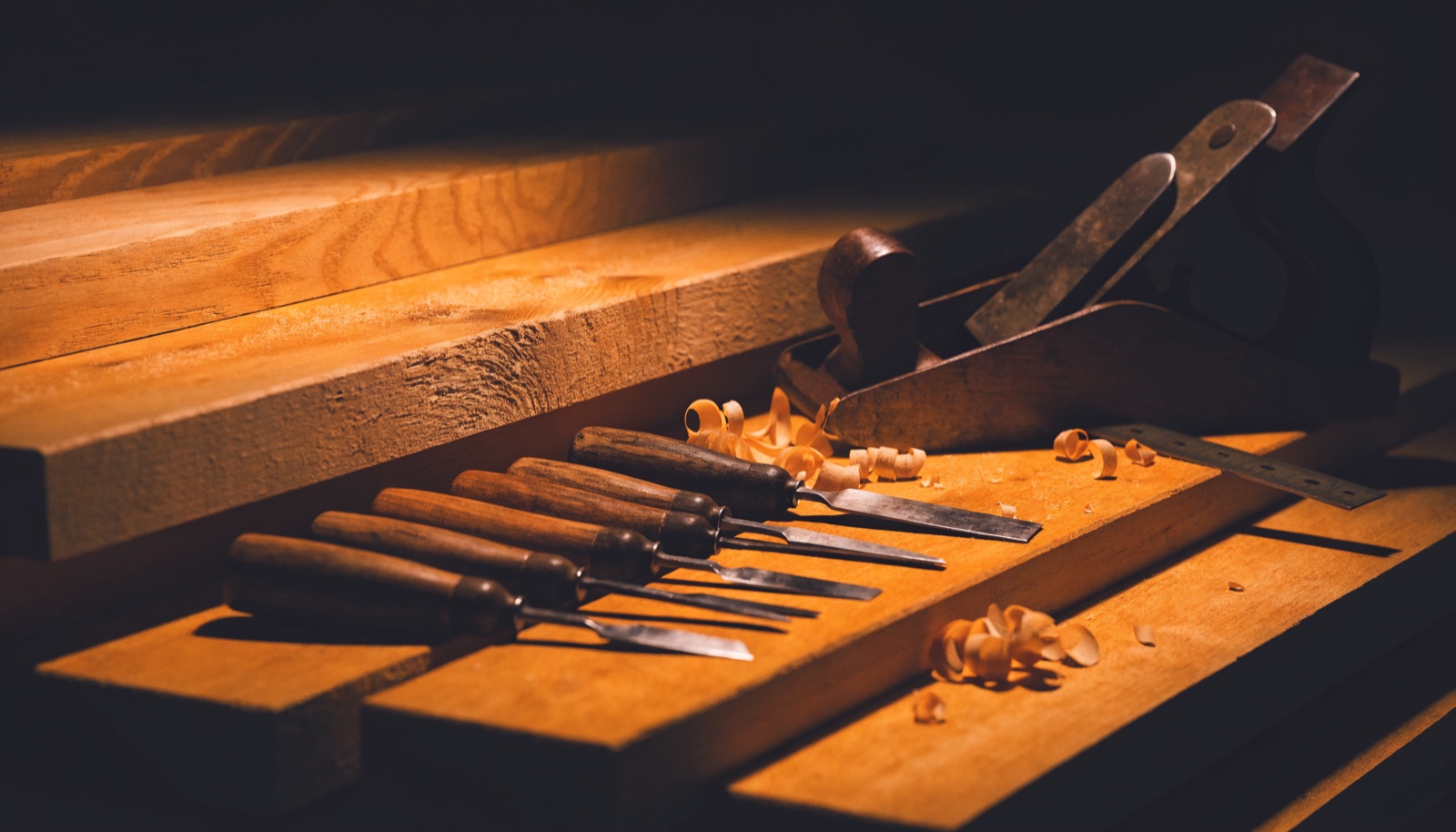 A row of wooden-handled chisels and a hand plane laid out on a timber bench