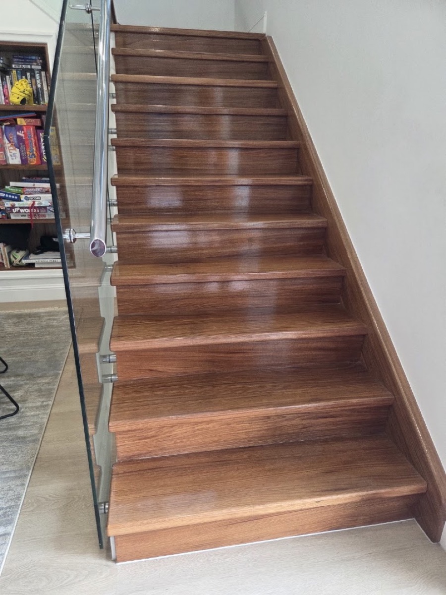 A polished timber staircase with a slim handrail turning up a wall