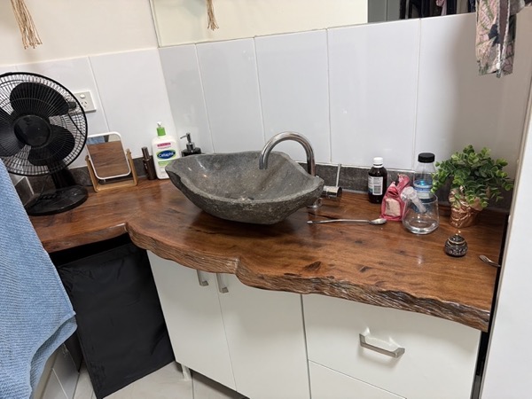 A live-edge timber vanity top with a stone basin set on it