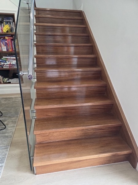 A polished timber staircase with a slim handrail turning up a wall