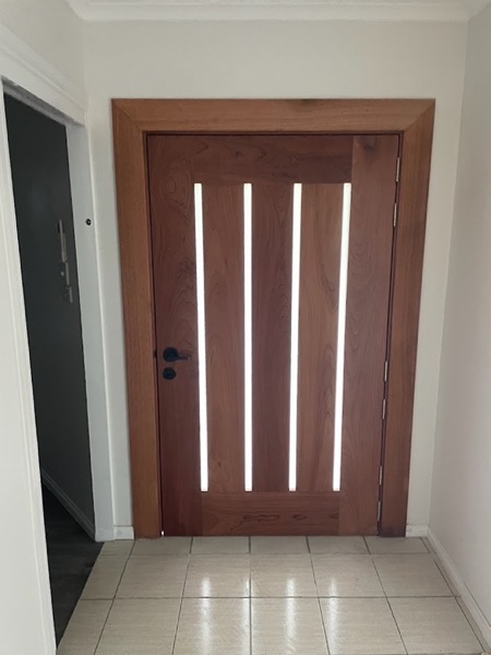 A dark stained timber door with four narrow vertical glazed slots