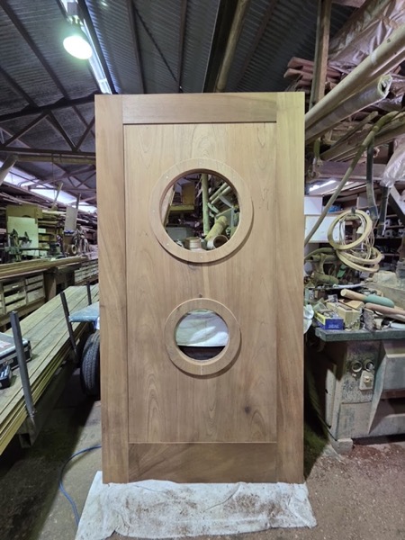 A timber door with two round glazed portholes standing in the workshop
