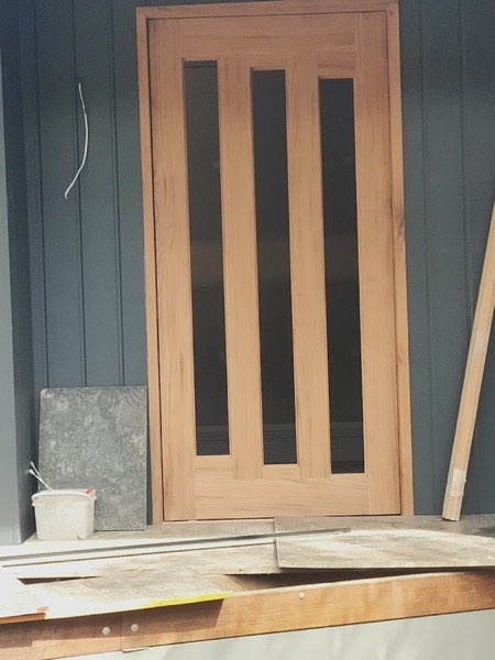 A timber door with tall vertical glazed panels standing against a painted wall