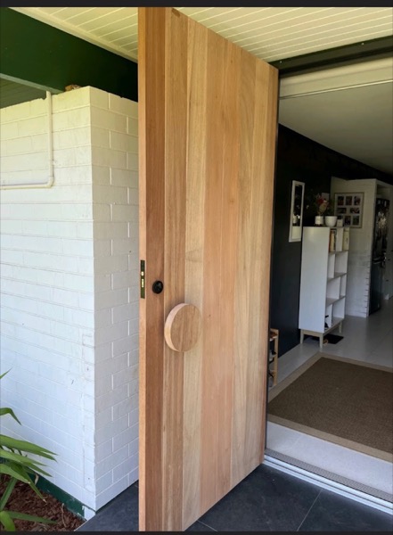A timber door with a round recessed detail set beside a doorway
