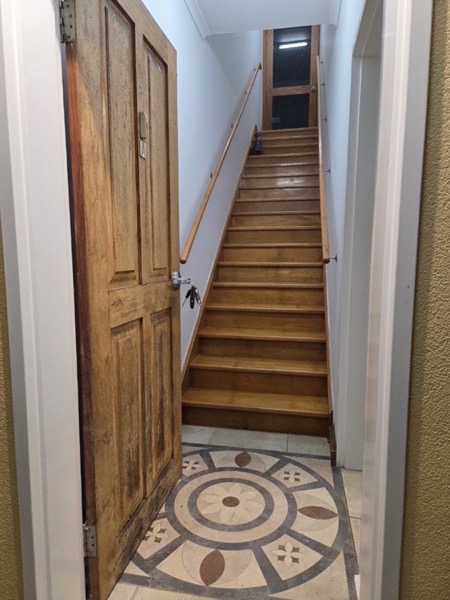 A panelled timber door standing at the foot of a timber staircase