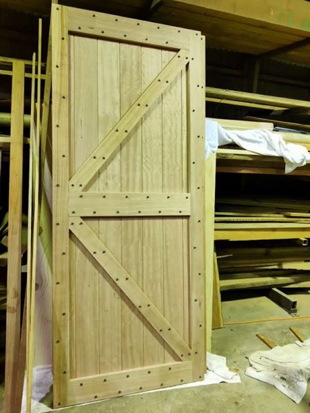 A ledged and braced timber door standing in the workshop under yellow light